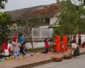 Monks handing out alms to people sitting at the side of a road in Luang Prabang, Laos.