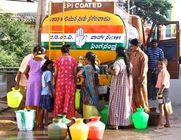 Women queuing to collect water from a tanker displaying a political message.